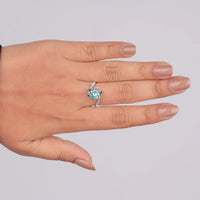 Hand wearing a ring with a blue gemstone on a light gray background