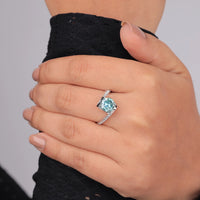 Hand wearing a ring with a blue gemstone on a plain background