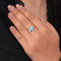 Hand wearing a ring with a blue gemstone on a dark background