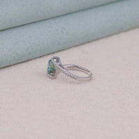 Silver ring with a green gemstone on a light pink surface