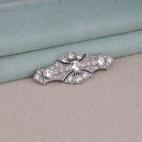 Art Deco vintage brooch featuring a round Cubic Zirconia center stone, blue accent stones, geometric design, and vintage-inspired styling.