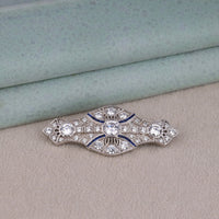 Art Deco vintage brooch featuring a round Cubic Zirconia center stone, blue accent stones, geometric design, and vintage-inspired styling.