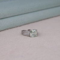 Asscher cut moissanite engagement ring with light green center stone, split shank pavé band, and elegant statement design