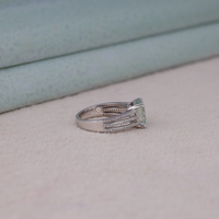 Asscher cut moissanite engagement ring with light green center stone, split shank pavé band, and elegant statement design