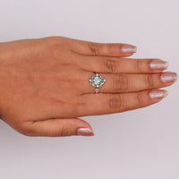 Green pear cut moissanite vintage engagement ring with decorative scrollwork accents and round accent stones