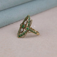 Gold ring with green gemstones on a beige surface