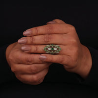 Hand wearing a decorative ring with green gemstones on a black background
