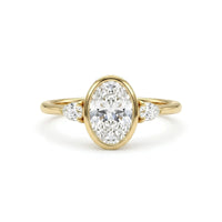 Oval cut Moissanite engagement ring with bezel-set 10.00 × 7.00 mm center stone, pear cut side stones, elegant yellow gold finish, and minimalist three-stone design.