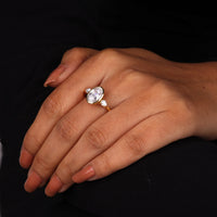 Oval cut Moissanite engagement ring with bezel-set 10.00 × 7.00 mm center stone, pear cut side stones, elegant yellow gold finish, and minimalist three-stone design.