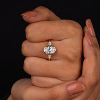 Oval cut Moissanite engagement ring with bezel-set 10.00 × 7.00 mm center stone, pear cut side stones, elegant yellow gold finish, and minimalist three-stone design.
