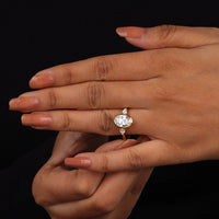 Oval cut Moissanite engagement ring with bezel-set 10.00 × 7.00 mm center stone, pear cut side stones, elegant yellow gold finish, and minimalist three-stone design.