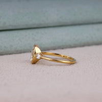 Oval cut Moissanite engagement ring with bezel-set 10.00 × 7.00 mm center stone, pear cut side stones, elegant yellow gold finish, and minimalist three-stone design.