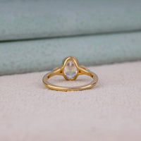 Oval cut Moissanite engagement ring with bezel-set 10.00 × 7.00 mm center stone, pear cut side stones, elegant yellow gold finish, and minimalist three-stone design.