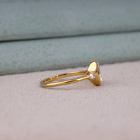 Oval cut Moissanite engagement ring with bezel-set 10.00 × 7.00 mm center stone, pear cut side stones, elegant yellow gold finish, and minimalist three-stone design.