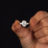 Oval cut Moissanite engagement ring with bezel-set 10.00 × 7.00 mm center stone, pear cut side stones, elegant yellow gold finish, and minimalist three-stone design.