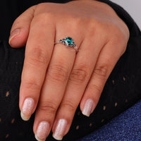 Pear cut green moissanite accent stone engagement ring with round black side stones in a prong setting
