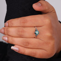Pear cut green moissanite accent stone engagement ring with round black side stones in a prong setting
