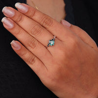 Pear cut green moissanite accent stone engagement ring with round black side stones in a prong setting