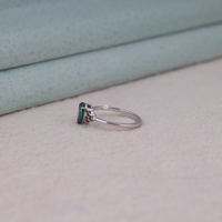 Pear cut green moissanite accent stone engagement ring with round black side stones in a prong setting