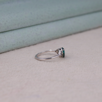 Pear cut green moissanite accent stone engagement ring with round black side stones in a prong setting