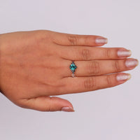 Pear cut green moissanite accent stone engagement ring with round black side stones in a prong setting