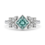 Princess cut moissanite engagement ring with aqua green center stone, leaf accent side stones, and nature-inspired design