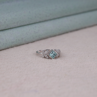 Princess cut moissanite engagement ring with aqua green center stone, leaf accent side stones, and nature-inspired design