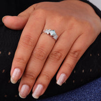Princess cut moissanite engagement ring with aqua green center stone, leaf accent side stones, and nature-inspired design