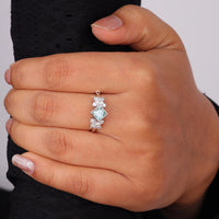 Princess cut moissanite engagement ring with aqua green center stone, leaf accent side stones, and nature-inspired design