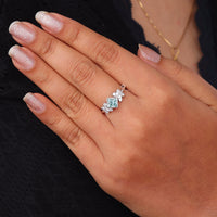 Princess cut moissanite engagement ring with aqua green center stone, leaf accent side stones, and nature-inspired design