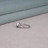 Princess cut moissanite engagement ring with aqua green center stone, leaf accent side stones, and nature-inspired design