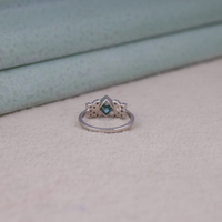 Princess cut moissanite engagement ring with aqua green center stone, leaf accent side stones, and nature-inspired design