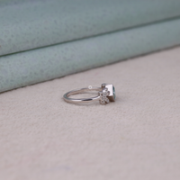 Princess cut moissanite engagement ring with aqua green center stone, leaf accent side stones, and nature-inspired design