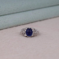 Vintage filigree statement ring featuring deep blue cabochon center stone with round accent stones and intricate scrollwork design