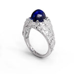 Vintage filigree statement ring featuring deep blue cabochon center stone with round accent stones and intricate scrollwork design