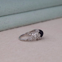 Vintage filigree statement ring featuring deep blue cabochon center stone with round accent stones and intricate scrollwork design