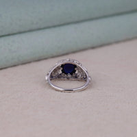 Vintage filigree statement ring featuring deep blue cabochon center stone with round accent stones and intricate scrollwork design