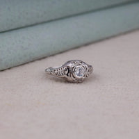 Vintage filigree engagement ring featuring a 5.00 mm round cut moissanite center stone in a decorative prong setting with intricate openwork design