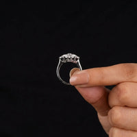 Hand holding a silver ring with a clear stone against a black background